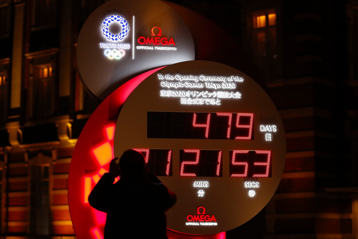 3月30日，行人在日本东京站前拍摄显示东京奥运会开幕式倒计时的电子钟，电子钟已根据新宣布的开幕时间进行调整。
