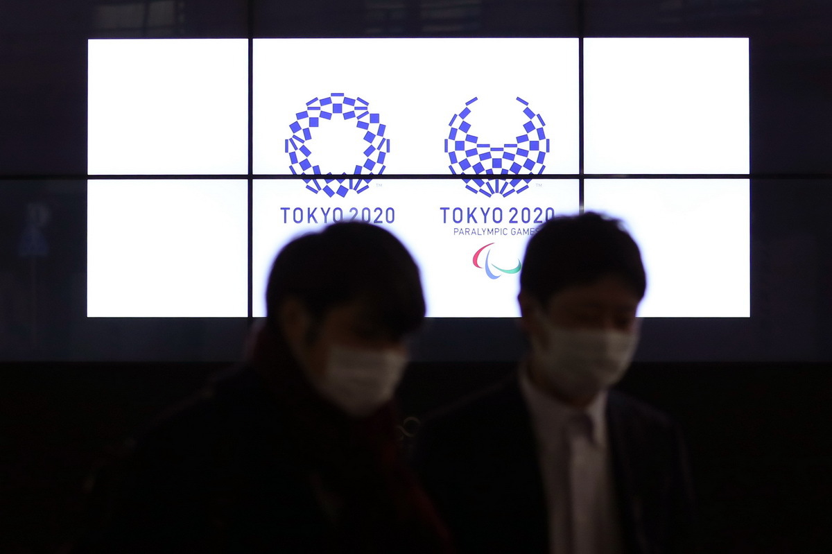 3月30日，在日本东京新桥，行人经过显示东京奥运会和残奥会会徽的电子屏。