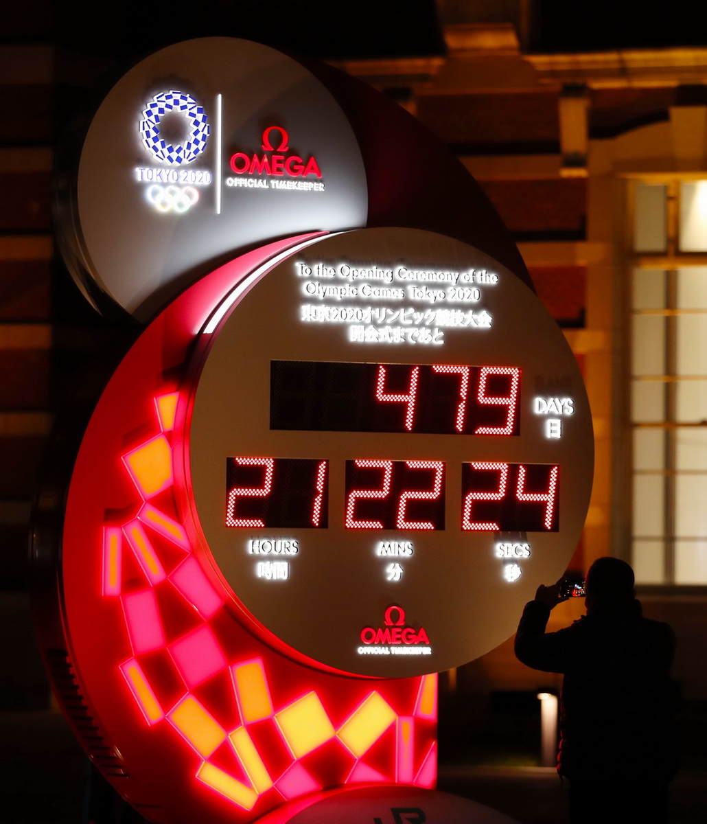 3月30日，行人在日本东京站前拍摄显示东京奥运会开幕式倒计时的电子钟，电子钟已根据新宣布的开幕时间进行调整。